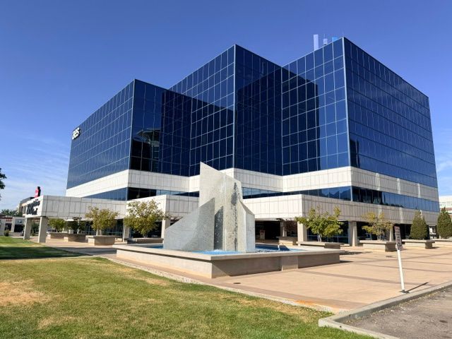 The blue-glass office tower at Parkview Plaza seen across the lawn, with the plaza’s stone fountain in front.